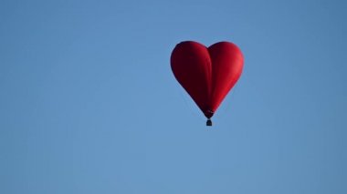 Gün batımında mavi gökyüzünde yavaş çekimde uçan renkli sıcak hava şekilli balon Sevgililer Günü konseptin kutlu olsun. 4k HDR Yüksek kalite görüntü