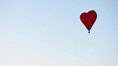 Gün batımında mavi gökyüzünde yavaş çekimde uçan renkli sıcak hava şekilli balon Sevgililer Günü konseptin kutlu olsun. 4k HDR Yüksek kalite görüntü