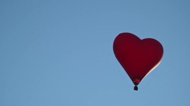Gün batımında mavi gökyüzünde yavaş çekimde uçan renkli sıcak hava şekilli balon Sevgililer Günü konseptin kutlu olsun. 4k HDR Yüksek kalite görüntü