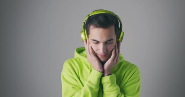 녹색 운동복을 입은 젊은 남성이 음악을 듣고 있습니다. 녹색 헤드폰을 쓰고 회색 배경 음악을 즐기는 남자 — 비디오