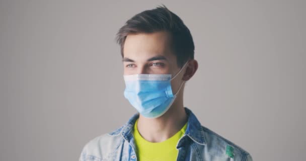 Giovane uomo in maschera medica tossisce e starnutisce da vicino. Studio girato su sfondo grigio — Video Stock