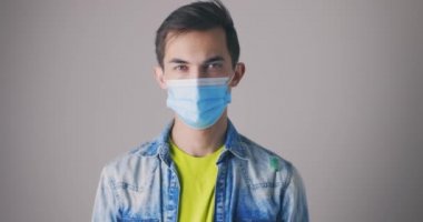 Mutlu genç erkek yüz koruyucu maskeyi çıkarır ve kameraya bakıp gülümser. Stüdyoda yakın plan portre. Virüs, salgın veya salgın konsepti.