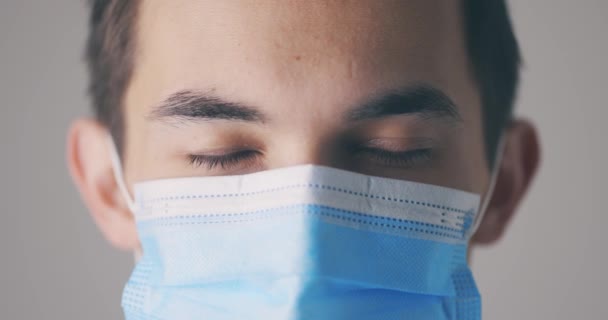 Giovane maschio in maschera medica che apre gli occhi e guarda dritto alla macchina fotografica. Ritratto ravvicinato in studio. Concetto virus. — Video Stock