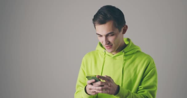 Utilização da internet móvel. Cara surpreso em rolar fotos em redes sociais, lendo notícias chocantes, assistindo blog com espanto. Estúdio interior filmado em fundo cinza — Vídeo de Stock