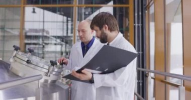 Bira fabrikasında çalışan iki Kafkasyalı adam. Bir erkek bira imalatçısı ölçümleri tablet kullanarak kontrol ediyor..