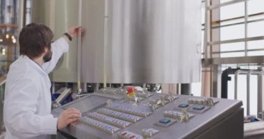 Bira fabrikasında sakallı bir erkek bira üreticisi kontrol panelinin arkasında çalışıyor.