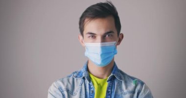 Gri arka planda koruyucu yüz maskesi takan genç bir adamın portresi. Stüdyo yakınlaştırması