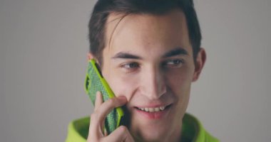 Yakından gülümseyen genç yakışıklı adam gri duvar arka planında telefonla konuşuyor. Yavaş çekimde konuşan çekici bir adam..