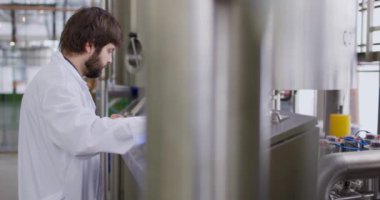 Bira fabrikasında sakallı bir erkek bira üreticisi kontrol panelinin arkasında çalışıyor.