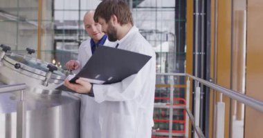 Bira fabrikasında çalışan iki Kafkasyalı adam. Bir erkek bira imalatçısı ölçümleri tablet kullanarak kontrol ediyor..