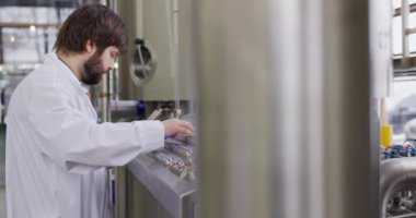 Bira fabrikasında sakallı bir erkek bira üreticisi kontrol panelinin arkasında çalışıyor.