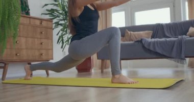 Sağlıklı ve güzel bir kadın evde egzersiz yapıyor oturma odasında esneme egzersizi yapıyor ve sabah sporunun tadını çıkarıyor. Yavaş çekim