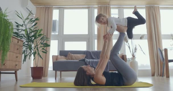 Fericit frumos familie sănătos tânără mama ridicarea drăguț copil fiica sus joc avion pe perete la domiciliu, amuzant copil fată care zboară în picioare mama practica acro pereche yoga lipire având distracție împreună — Videoclip de stoc