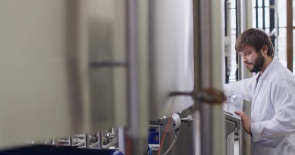 Bira fabrikasında sakallı bir erkek bira üreticisi kontrol panelinin arkasında çalışıyor. — Stok video