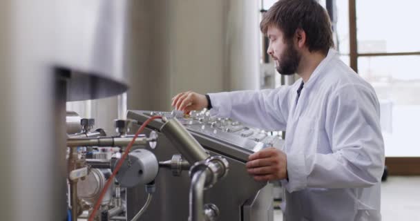 Seorang laki-laki pembuat bir dengan jenggot di pabrik pembuatan bir bekerja di belakang panel kontrol, dashboard — Stok Video