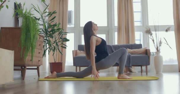 Приваблива молода активна жінка займається розтягуванням йоги на килимку вдома. Здорове життя, дотримуйтесь концепцій. Повільний рух — стокове відео