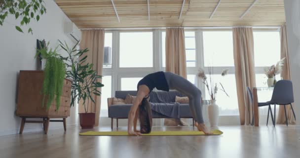 O femeie sănătoasă și frumoasă care exercită acasă practicând întinderea în camera de zi bucurându-se de exerciții de fitness de dimineață. Slow motion — Videoclip de stoc