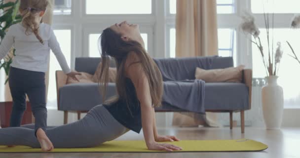 Młoda piękna kobieta i jej dziewczynka trenują jogę rozciągającą się w domu. Mama gra w fitness z córką. Zwolniony ruch — Wideo stockowe