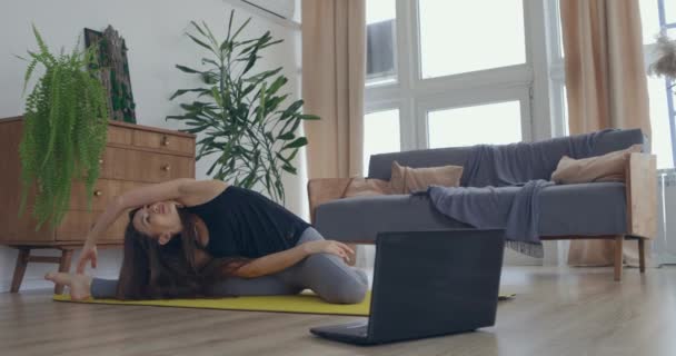 Aantrekkelijke jonge actieve vrouw die online stretching yoga lessen thuis, kijken tutorial op laptop. Gezond leven, fit blijven concepten — Stockvideo