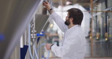Bira fabrikası işçisi. Bira tanklarının yanındaki fabrikada laboratuvar önlüğü giymiş bir adam.