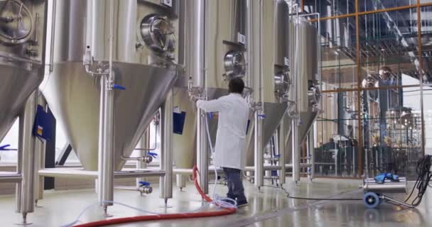 Brouwerij werknemer in het arbeidsproces. Man gekleed in labjas in brouwerij fabriek in de buurt van biertanks — Stockvideo