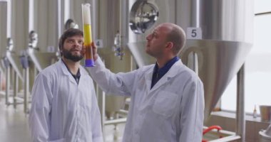 Bira fabrikasında taze biranın kalitesini test eden iki adam. Laboratuvar önlüğü giymiş biracılar bira tadıyor ve tartışıyorlar..
