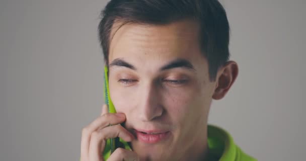 Detailní úsměv mladý pohledný muž mluví telefon emocionálně na šedé zdi pozadí. Atraktivní muž mluví mobilní telefon ve zpomaleném filmu. — Stock video