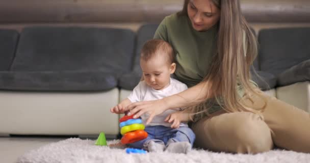 Happy young mother and child boy play together with pyramid indoors at home. Mom and baby toddler playing and having fun time together. — Stock Video