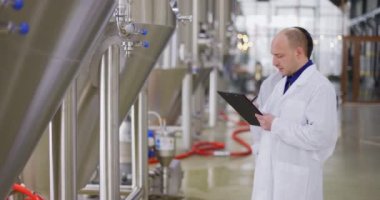 Bira fabrikasında çalışan iki Kafkasyalı adam. Bir erkek bira imalatçısı ölçümleri tablet kullanarak kontrol ediyor..