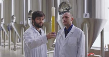 Bira fabrikasında taze biranın kalitesini test eden iki adam. Laboratuvar önlüğü giymiş biracılar bira tadıyor ve tartışıyorlar..