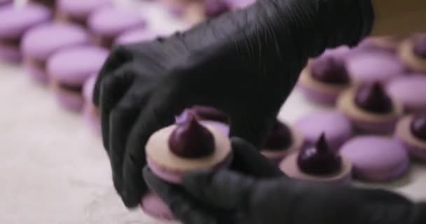 Proceso de hacer macarrón macaroon, postre francés. Montaje de dos mitades con relleno. Manos en guantes negros — Vídeos de Stock