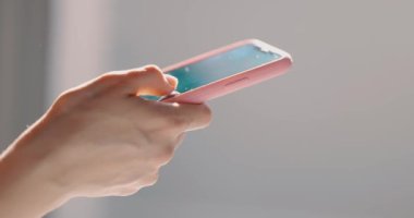 Yatak odasında akıllı telefon kullanan ve mesaj yazan bir kız. Genç kadınların elinin yakın çekimi. Yan görünüm.
