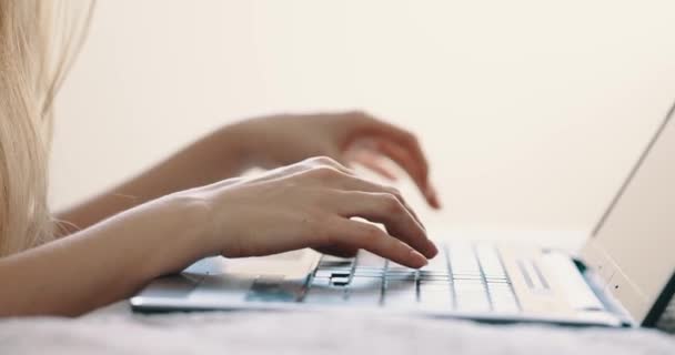 Mãos femininas digitando no teclado do laptop na cama no quarto, vista de perto. Luz solar brilhante — Vídeo de Stock