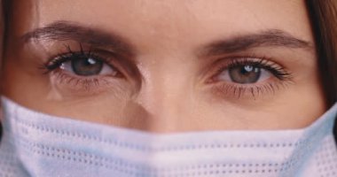 Kadın gözlerinin portresini kapat. Tıbbi maskeli kadın kameraya bakar, makro çekim.
