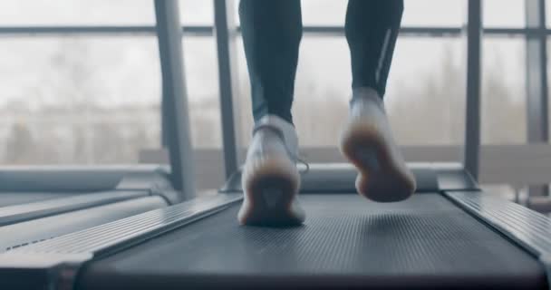 Close-up atletische voeten lopen op loopband in de fitnessruimte, slow motion. Achteraanzicht van witte sneakers die trainen op de loopband. Weinig zicht op mannenbenen training in sportclub — Stockvideo