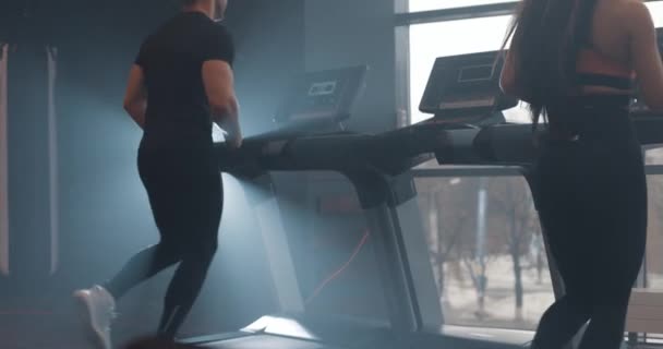 Kobieta i mężczyzna biegający na bieżni na siłowni. Poniżej zobaczyć nogi sportowców, zwolnione tempo — Wideo stockowe
