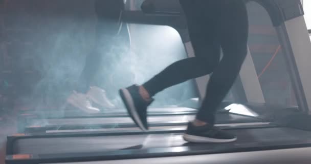 Kobieta i mężczyzna biegający na bieżni na siłowni. Poniżej zobaczyć nogi sportowców, zwolnione tempo — Wideo stockowe