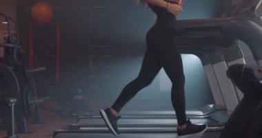 Spor kıyafetleriyle spor salonunda koşu bandında ağır çekimde koşan çekici genç bir kadının yan görüntüsü.