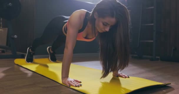 Mladá atraktivní fitness žena provádí kliky na podložce ve sportovním klubu nebo tělocvičně. Sexy štíhlé sportovní dívka v černém sportovním oblečení dělá warm-up cvičení, zpomalený pohyb — Stock video