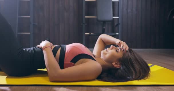 Vista lateral joven hermosa mujer en forma se encuentra agotado. Mujer atractiva extremadamente cansada en el gimnasio descansando — Vídeos de Stock