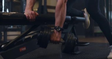 Yakışıklı, üstsüz, kaslı vücut geliştirme sporcusu spor salonunda sırt kaslarını geliştiren ağırlık egzersizi. Vücut geliştirici dambılı kaldırır, yavaş çekimde.