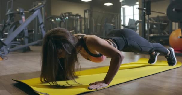 Genç çekici fitness kadını bir spor kulübünde ya da spor salonunda şınav çekiyor. Siyah spor giysili seksi, ince atletik kız ısınma egzersizleri yapıyor, yavaş çekim. — Stok video