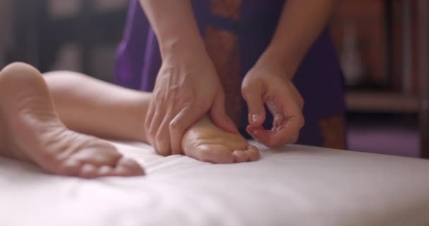 No salão de beleza. Profissional massagista do sexo feminino mãos massageando pés de mulher deitada relaxante. Massagem de acupressão nos pés no centro de spa médico. Movimento lento — Vídeo de Stock