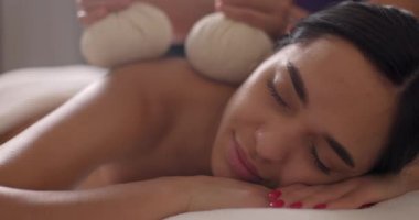 Genç çekici esmer kadın terapi sırasında dinleniyor sırtına bitkisel spa topu takıyor ve kaplıca salonuna masaj yapıyor..