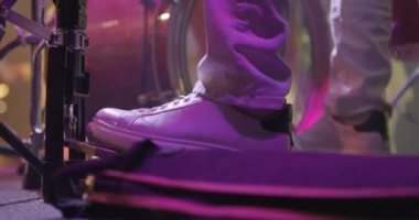 Sahnede spor ayakkabılı bir davulcunun bacaklarına yakın çekim. Davulcu bas davul pedalını tekmeliyor. Backgound 'daki müzik grubu, canlı konser. Yavaş çekim