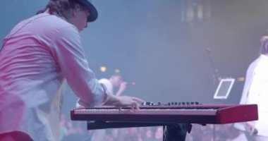 Man Musician 'ın arka planı konserde Sentezleyici' yi çalıyor. Parlak Sahne Işığı. Arka planda kadın vokalist. Yavaş çekim.