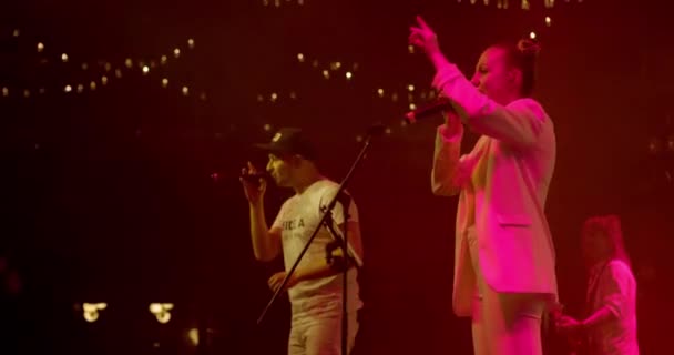 Mujer cantante, vista lateral de una cantante con luces de escenario. Joven mujer elegante cantando canción en concierto en vivo, cantando hombre en el fondo. Movimiento lento — Vídeos de Stock