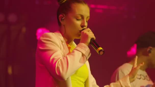 Νεαρή τραγουδίστρια με λευκά ρούχα τραγουδά συναισθηματικά και κινείται στη σκηνή σε ζωντανή συναυλία. Φωτεινό φως στάδιο — Αρχείο Βίντεο