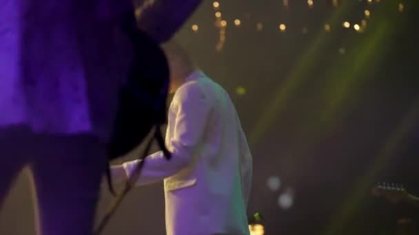 Back view of young woman singer in white clothes emotionally sings and moves on the stage at live concert. Bright stage light — Stock Video