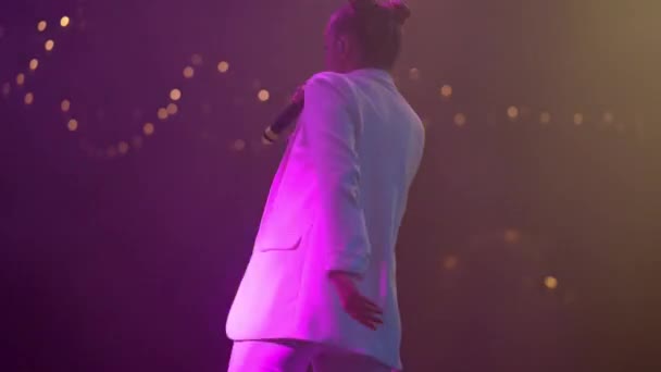 白い服を着た若い女性歌手が感情的に歌い、ライブコンサートでステージに移動します。明るいステージライト — ストック動画